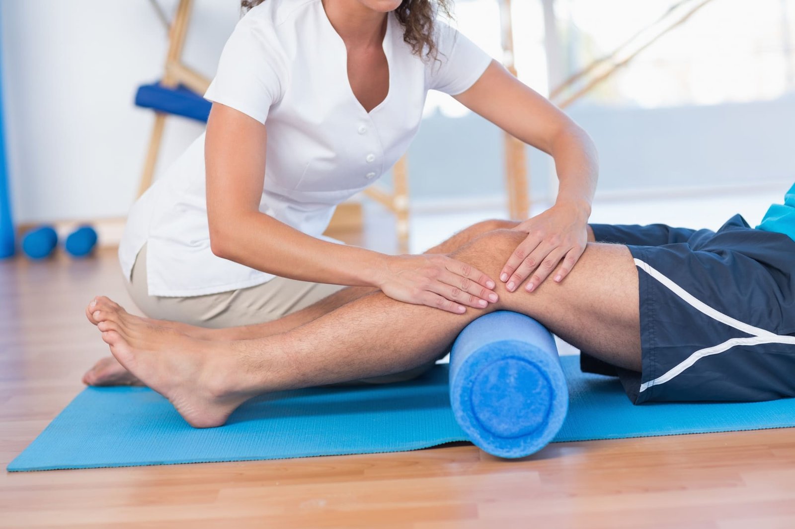 Physiotherapeutin behandelt das Knie eines Patienten mit einer Faszienrolle